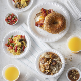 breakfast bagel sandwich, scrambled eggs, and grits in different size white bowls and plates