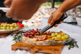 charcuterie catering platter with grapes, meats, and cheese and black serving tongs