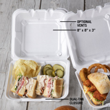 white takeout container with a turkey club sandwich with potato chips and pickles inside