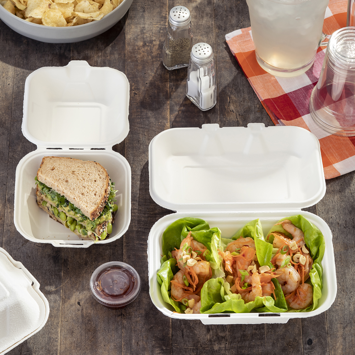 small half vegetarian sandwich and three shrimp lettuce wraps in two different sized takeout containers on a dining table	