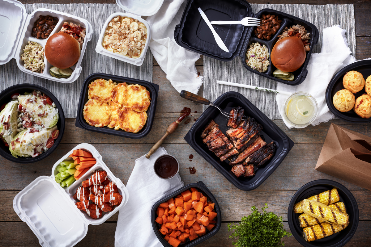 variety of hot foods in takeout packaging on a dining table