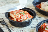 lasagna in a black takeout container with a clear lid	