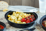 gnocchi with fresh tomatoes in a round black takeout container with clear lid