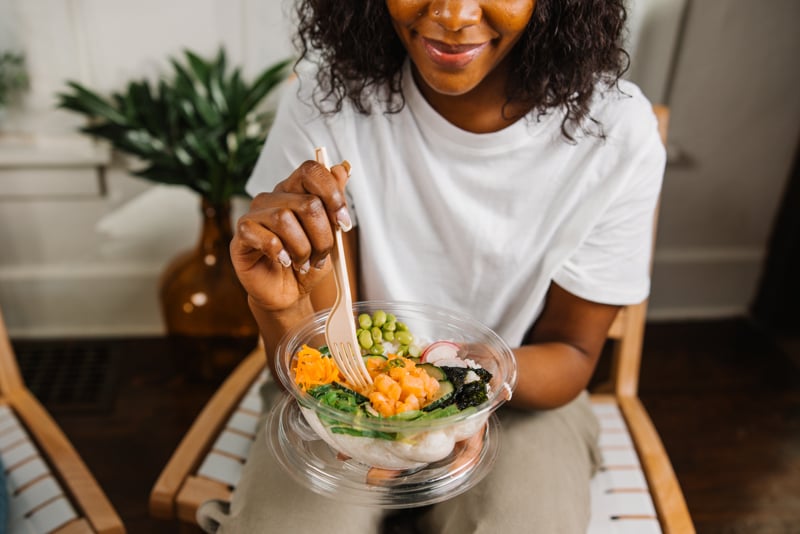 Woman beginning to eat a poke bowl in a round clear container