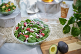 large salad in a clear catering container with black serving tongs	