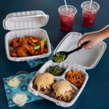 chicken wings in a takeout container with celery and carrots and two chicken sandwiches in a takeout container with divider sections	