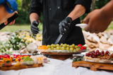 three different size clear catering platters one with fresh sliced veggies, one with fresh fruits, and one with nuts and crackers	