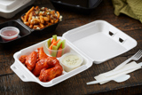 white takeout container with spicy chicken wings with celery, carrots, and blue cheese sauce in a portion cup inside	