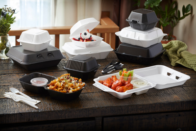 loaded fries, spicy chicken wings, and a strawberry dessert in takeout containers sitting on a dining table