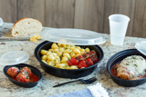 gnocchi with fresh tomatoes in a round black takeout container with clear lid