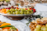 three different size clear catering platters one with fresh sliced veggies, one with fresh fruits, and one with nuts and crackers	