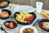 gnocchi with fresh tomatoes in a round black takeout container with clear lid