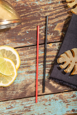 a red disposable straw and a black disposable draw laying next to each other on a wooden table