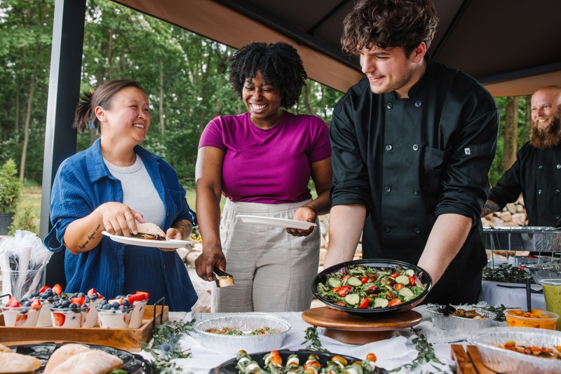 four people standing by fresh food in catering style containers