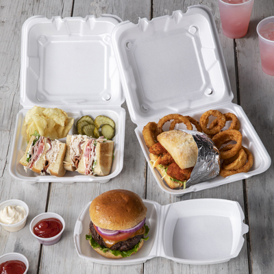 three different white takeout containers, one with a turkey club sandwich with potato chips and pickles inside, one with a fried chicken sandwich and onion rings, and one with a cheeseburger