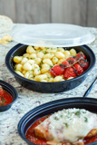 gnocchi with fresh tomatoes in a round black takeout container with clear lid