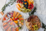 three different size clear catering platters one with fresh sliced veggies, one with fresh fruits, and one with nuts and crackers	