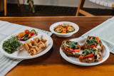 chicken kebabs, sliced veggies, cucumber and carrot salad, and vegetarian toast on different kinds of compostable plates	