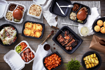 variety of hot foods in takeout packaging on a dining table	