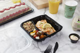 salmon entree in a hinge lid take out container with compartments for the entree and two sides