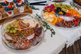 three different size clear catering platters one with fresh sliced veggies, one with fresh fruits, and one with nuts and crackers	