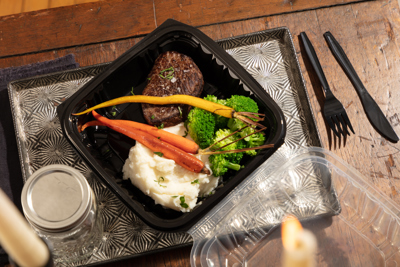 dinner food at a dining table in a two piece takeout container