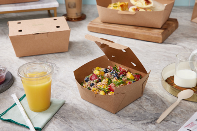 fresh salad in a square shape brown takeout container with a side of cold orange juice in a clear cup