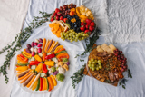 three different size clear catering platters one with fresh sliced veggies, one with fresh fruits, and one with nuts and crackers	