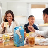 family enjoying breakfast together with a milk carton in the forefront	